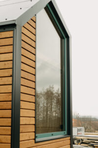Hliníková okna na fasádě mobilního tiny house – černý rám kontrastující s přírodní dřevěnou konstrukcí v exteriéru.