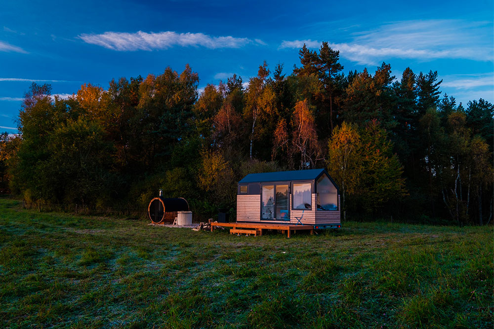 Moderní maringotka od Woodky.cz s dřevěným obkladem, velkým oknem a mobilním podvozkem, ideální jako chata nebo tiny house.